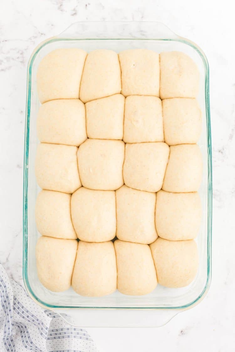 Proofed dinner roll dough in a glass baking pan.