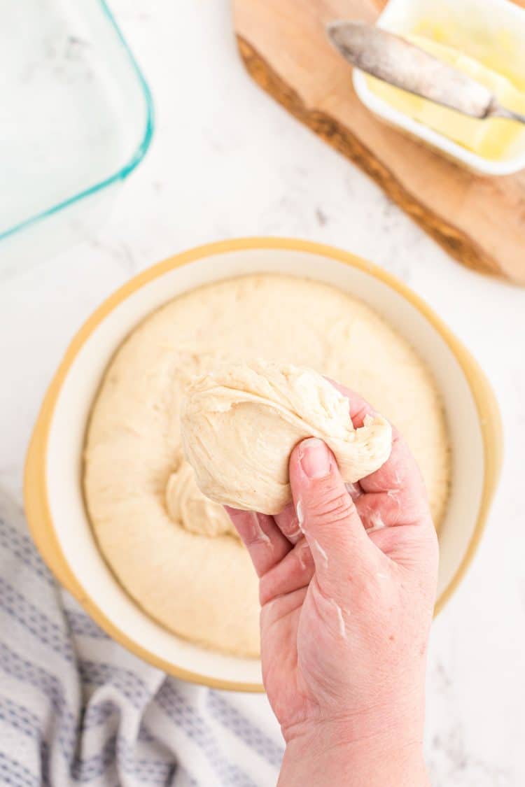 A woman's hand pulling dough out of a bowl to make dinner rolls.