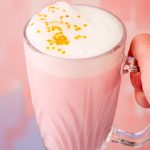 Close up photo of a woman's hand holding a mug of pink angel milk.