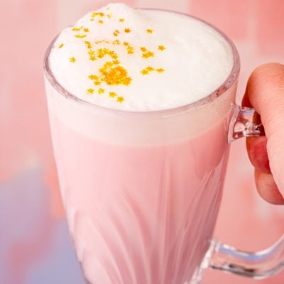 Close up photo of a woman's hand holding a mug of pink angel milk.