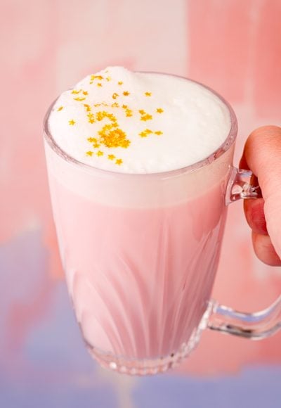 Close up photo of a woman's hand holding a mug of pink angel milk.