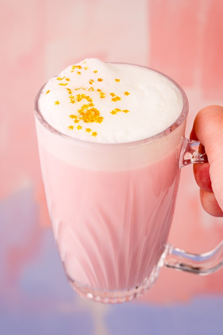 Close up photo of a woman's hand holding a mug of pink angel milk.