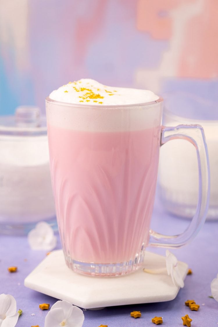 Close up photo of a mug filled with pink angel milk on a purple surface.