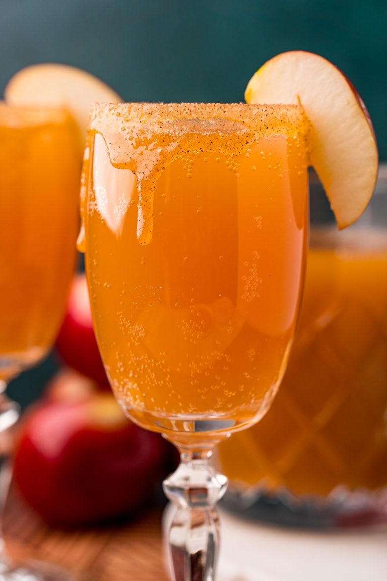 Close up photo of an apple cider mimosa in a glass garnished with an apple slice.