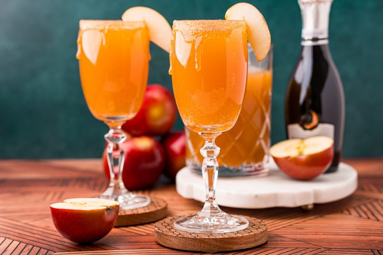 Close up photo of an apple cider mimosa in a glass garnished with an apple slice.