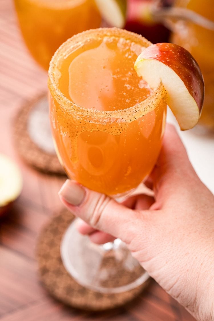 A woman's hand holding an apple cider mimosa close to the camera.