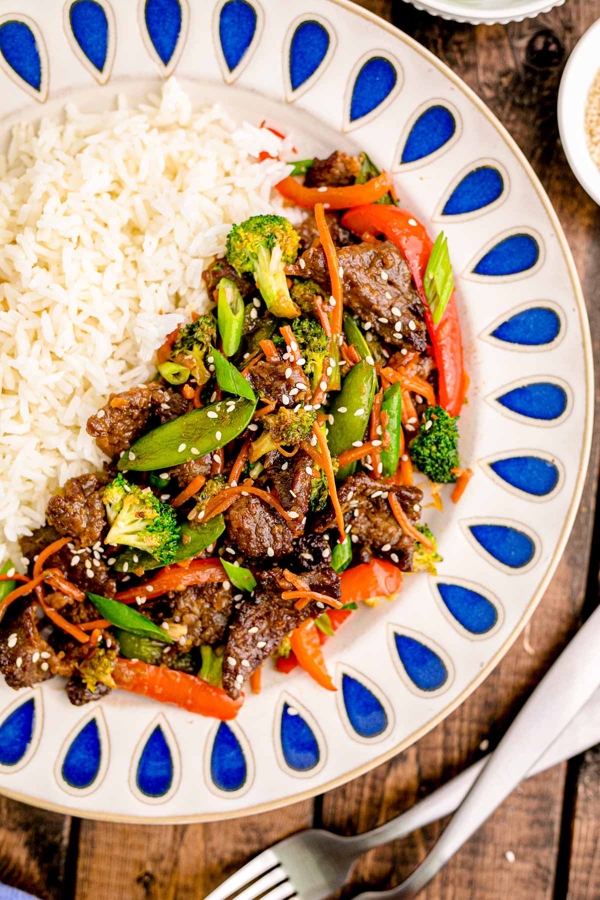Beef stir fry on a white and blue plate with white rice.