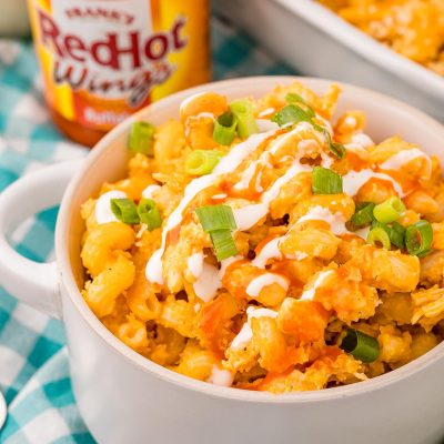 Close up photo of a bowl of buffalo chicken mac and cheese on a teal and white gingham napkin.