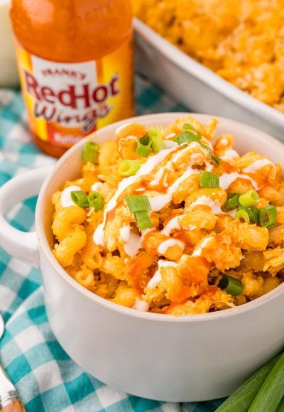 Close up photo of a bowl of buffalo chicken mac and cheese on a teal and white gingham napkin.