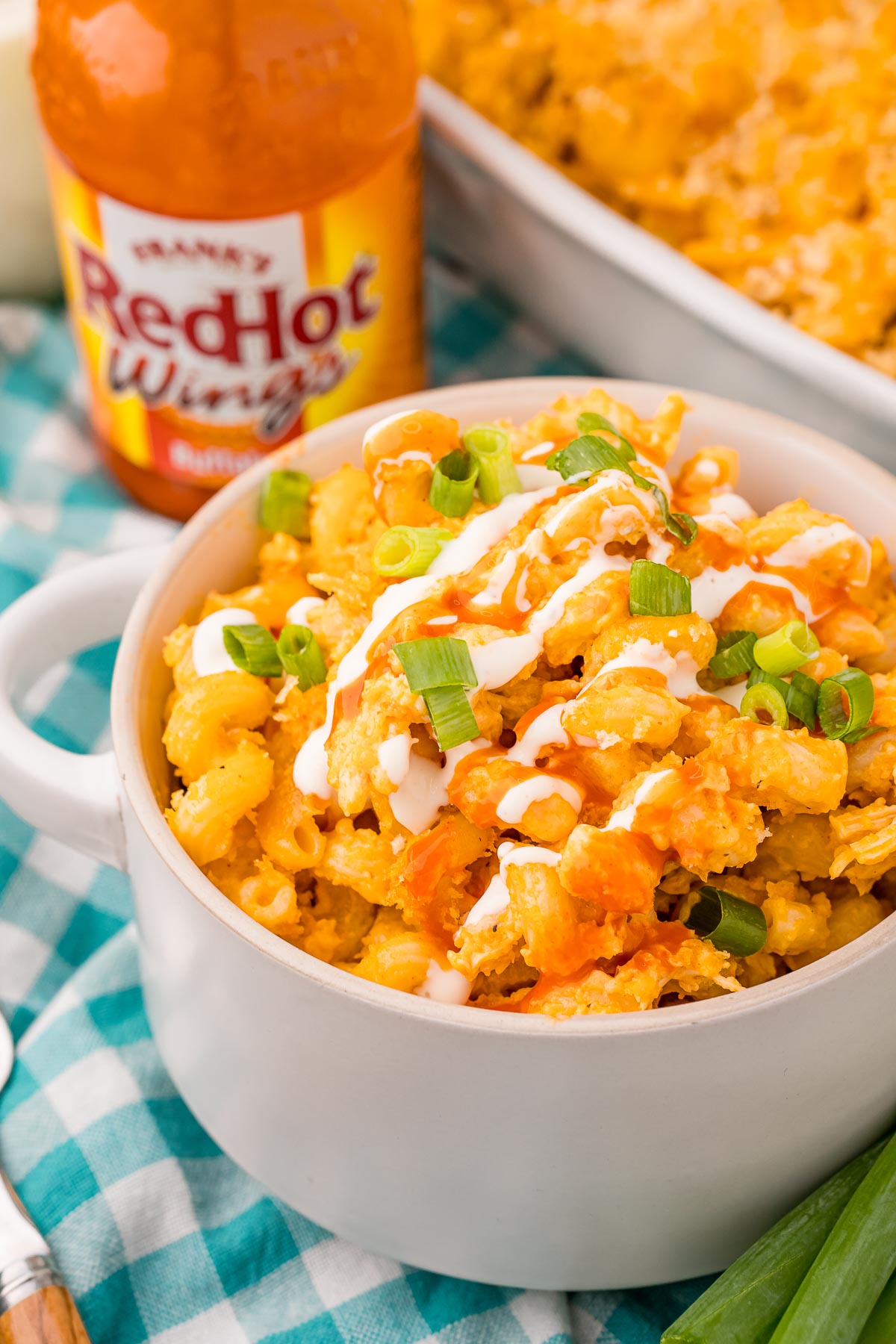 A bowl of buffalo chicken mac and cheese with a bottle of buffalo sauce in the background.