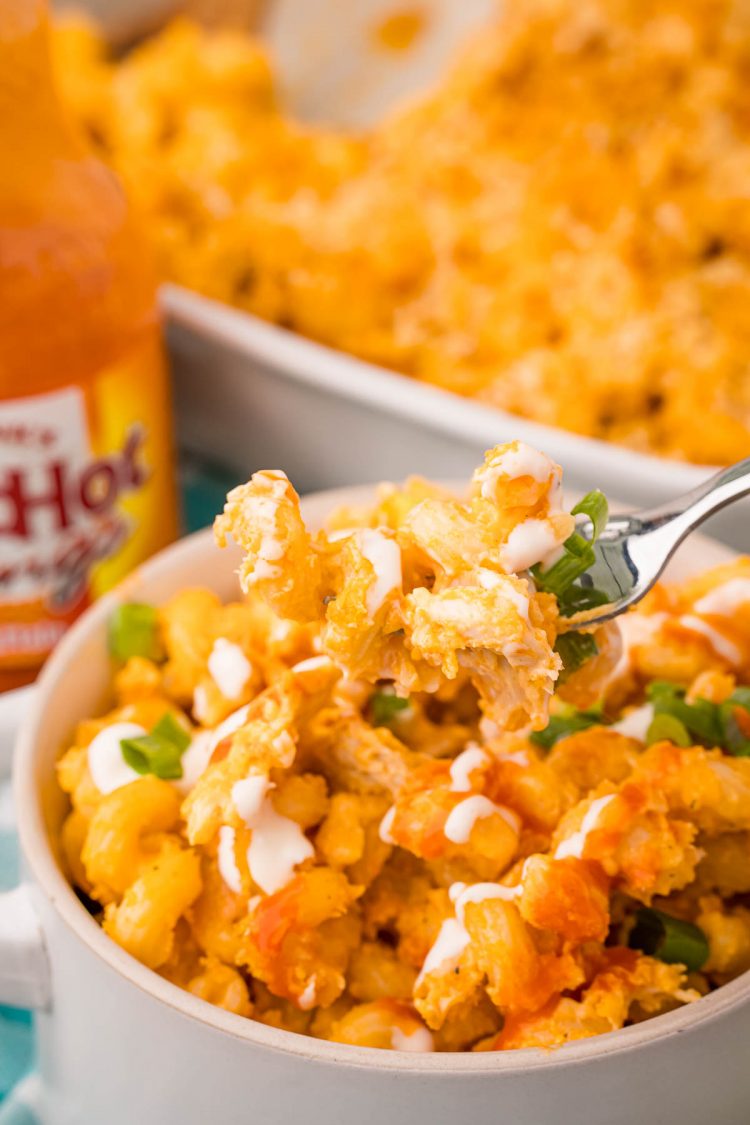 A fork taking a bite of buffalo mac and cheese out of a bowl.