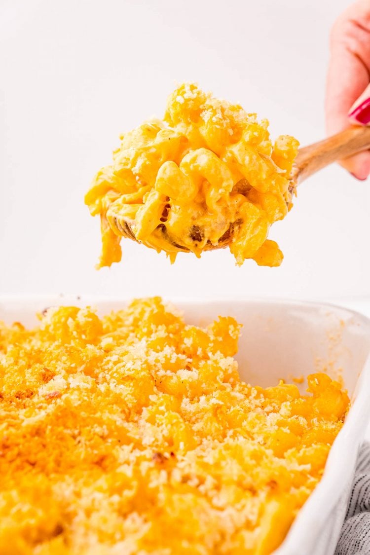 Close up photo of a serving spoon scooping buffalo chicken mac and cheese out of a white casserole dish.