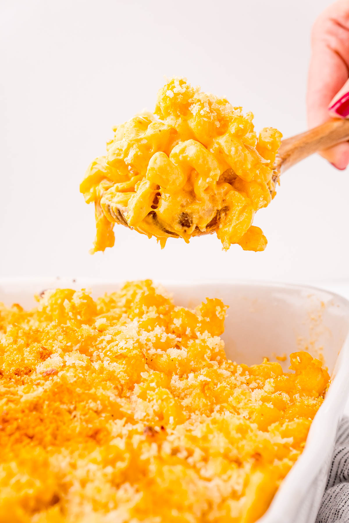 Close up photo of a serving spoon scooping buffalo chicken mac and cheese out of a white casserole dish.
