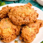 Close up photo of buttermilk fried chicken on a white plate on a teal napkin.