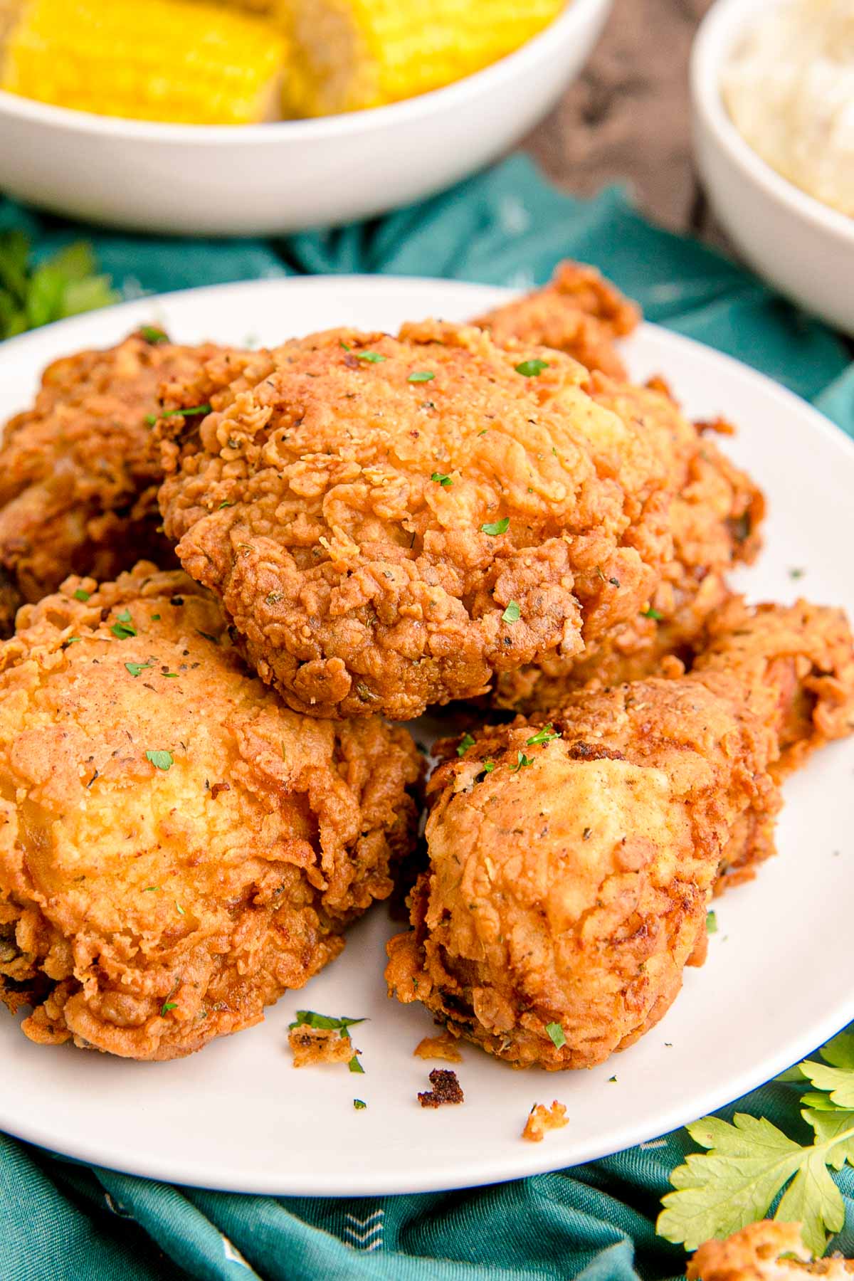 Close up photo of buttermilk fried chicken on a white plate on a teal napkin.