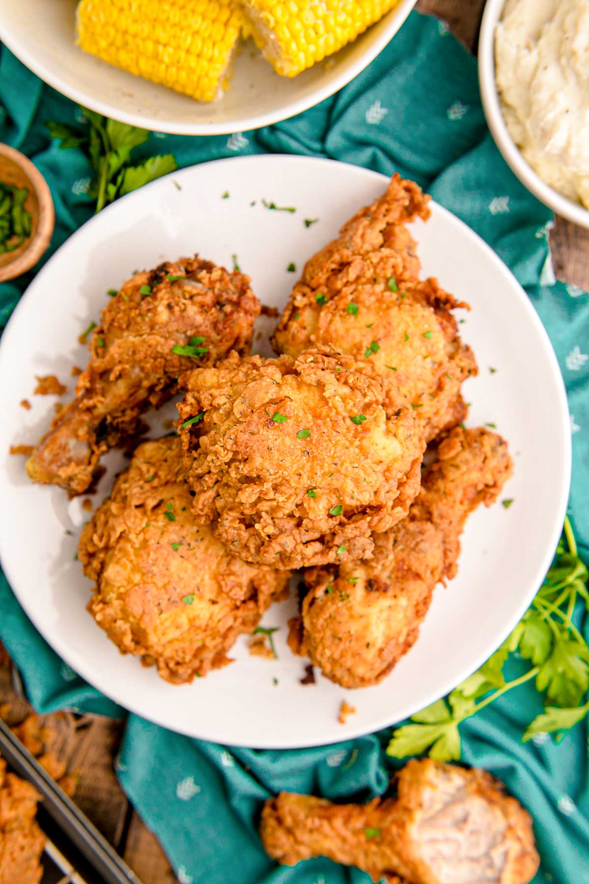 Overhead photo of fried chicken on a white plate on a teal napkin.