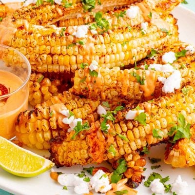 Close up photo of a large white plate with corn ribs on it on a teal surface.