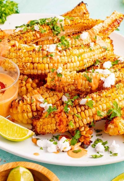 Close up photo of a large white plate with corn ribs on it on a teal surface.