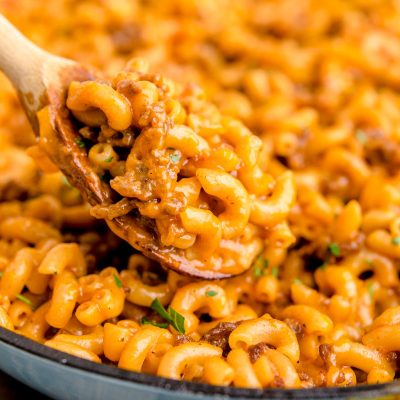 Close up photo of a wooden spoon scooping hamburger helper out of a skillet.