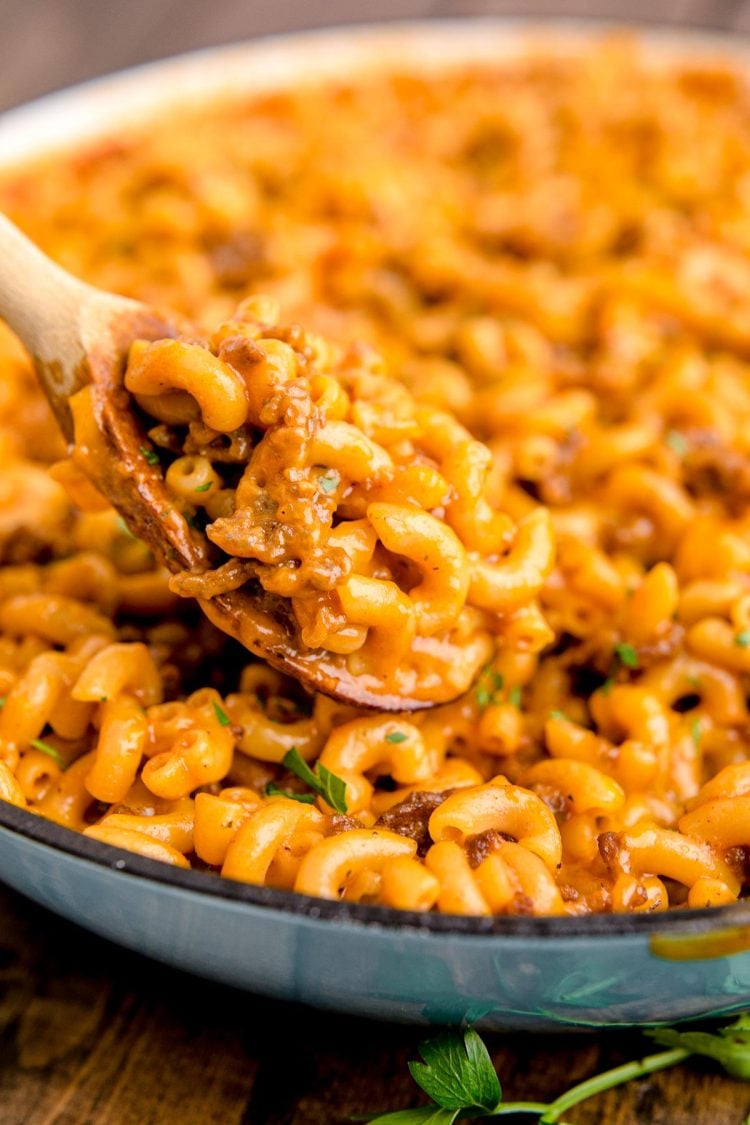 Close up photo of a wooden spoon scooping hamburger helper out of a skillet.