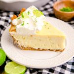 Close up photo of a slice of key lime pie on a white plate on a black and white checkered napkin.