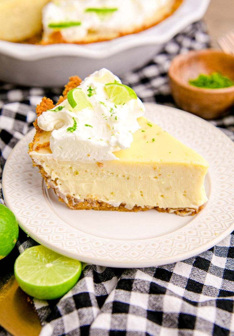 Close up photo of a slice of key lime pie on a white plate on a black and white checkered napkin.