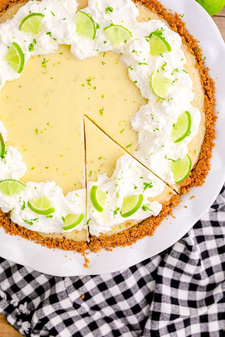 Close up overhead photo of a key lime pie in a white pie dish on a black and white gingham napkin.