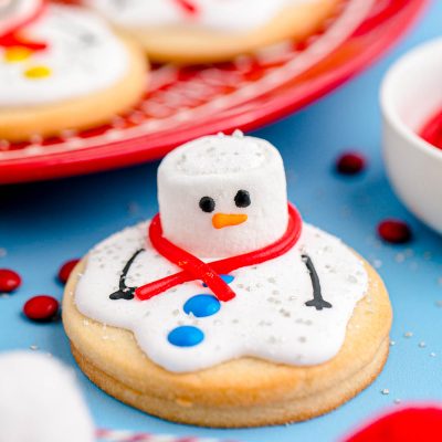 Close up photo of melted snowman cookies on a blue counter with some on a red plate in the background.