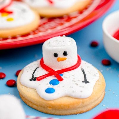 Close up photo of melted snowman cookies on a blue counter with some on a red plate in the background.