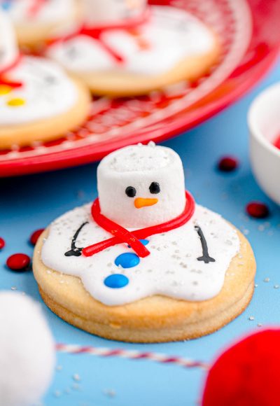 Close up photo of melted snowman cookies on a blue counter with some on a red plate in the background.