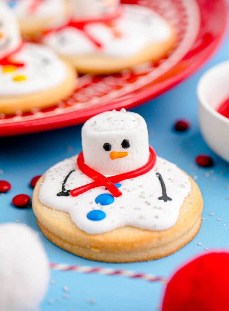 Close up photo of melted snowman cookies on a blue counter with some on a red plate in the background.