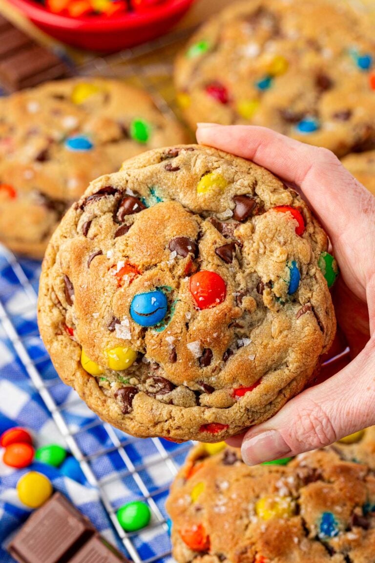 A woman's hand holding a large M&M monster cookie to the camera.