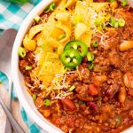 Overhead photo of a bowl of slow cooker chili on a teal gingham napkin.