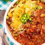 Overhead photo of a bowl of slow cooker chili on a teal gingham napkin.