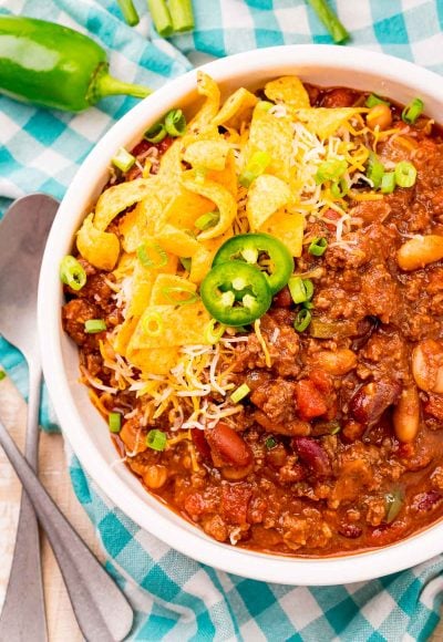Overhead photo of a bowl of slow cooker chili on a teal gingham napkin.