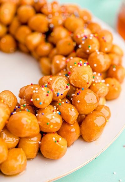 Close up photo of struffoli on a white plate on a mint green surface.