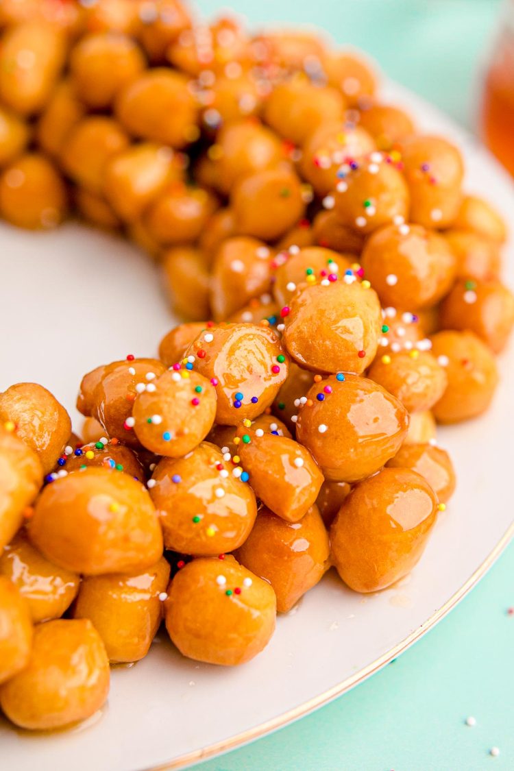 Close up photo of struffoli on a white plate on a mint green surface.