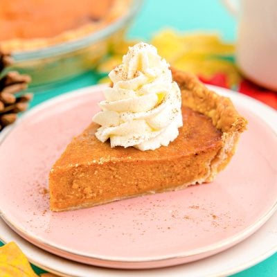 Close up photo of a slice of air fryer pumpkin pie on a pink plate with the rest of the pie in the background.