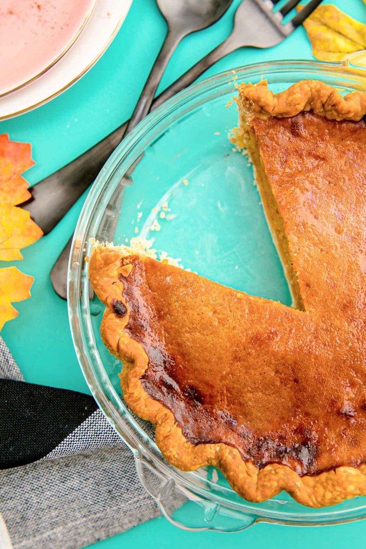 Overhead photo of a pumpkin pie in a glass baking dish with a slice missing.