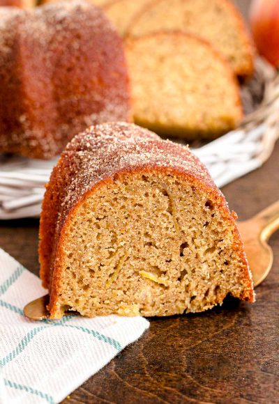 Close up photo of a slice of apple cider donut cake on a cake server on a wooden table.