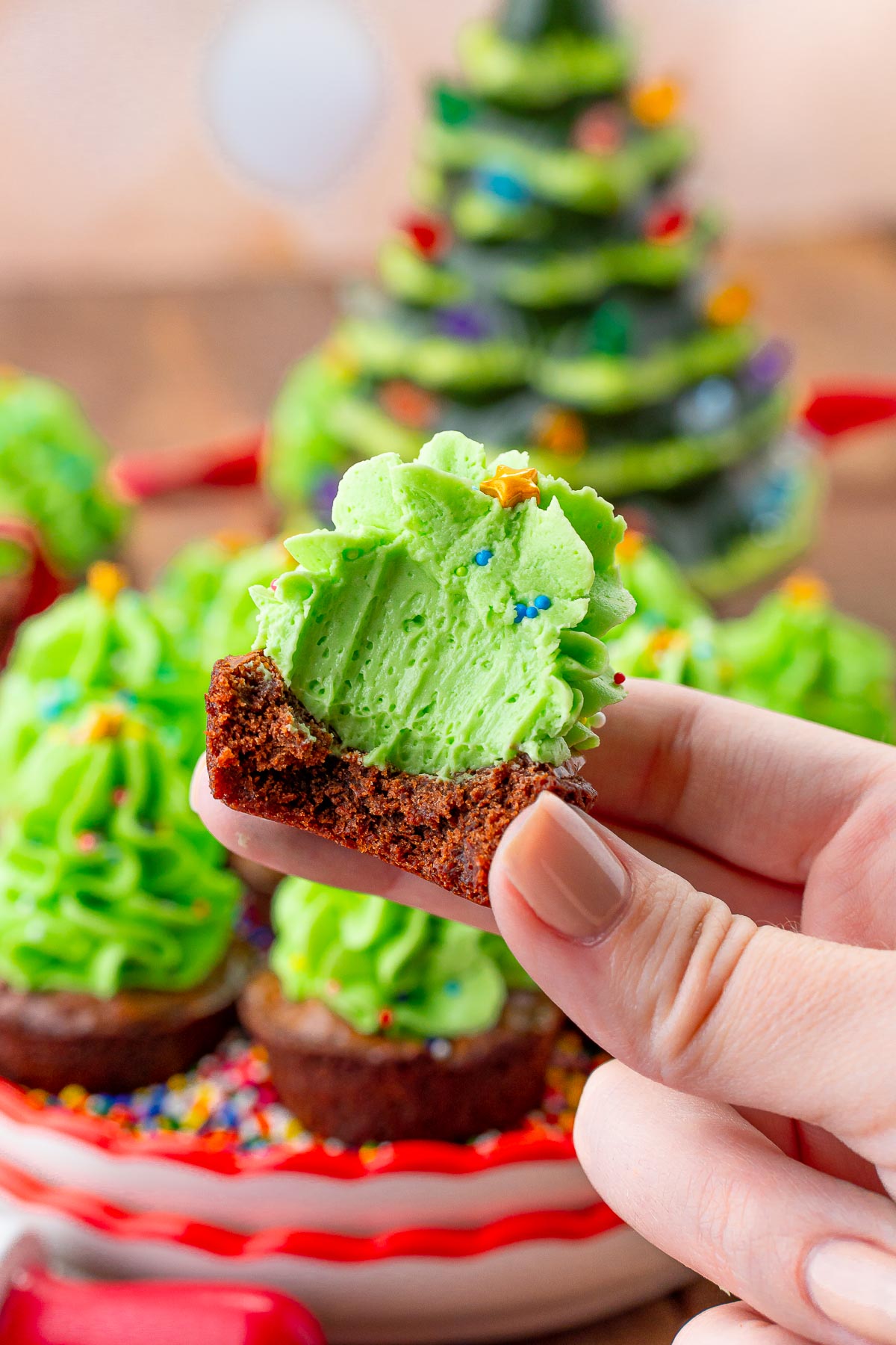 A woman's hand holding a christmas tree brownie bite that has a bite taken out of it.
