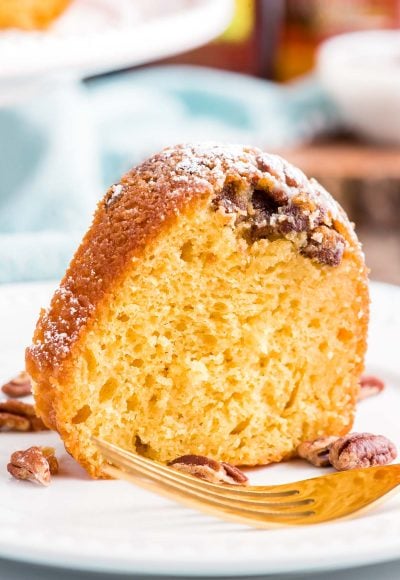 Close up photo of a slice of rum cake on a white plate with a blue napkin in the background.