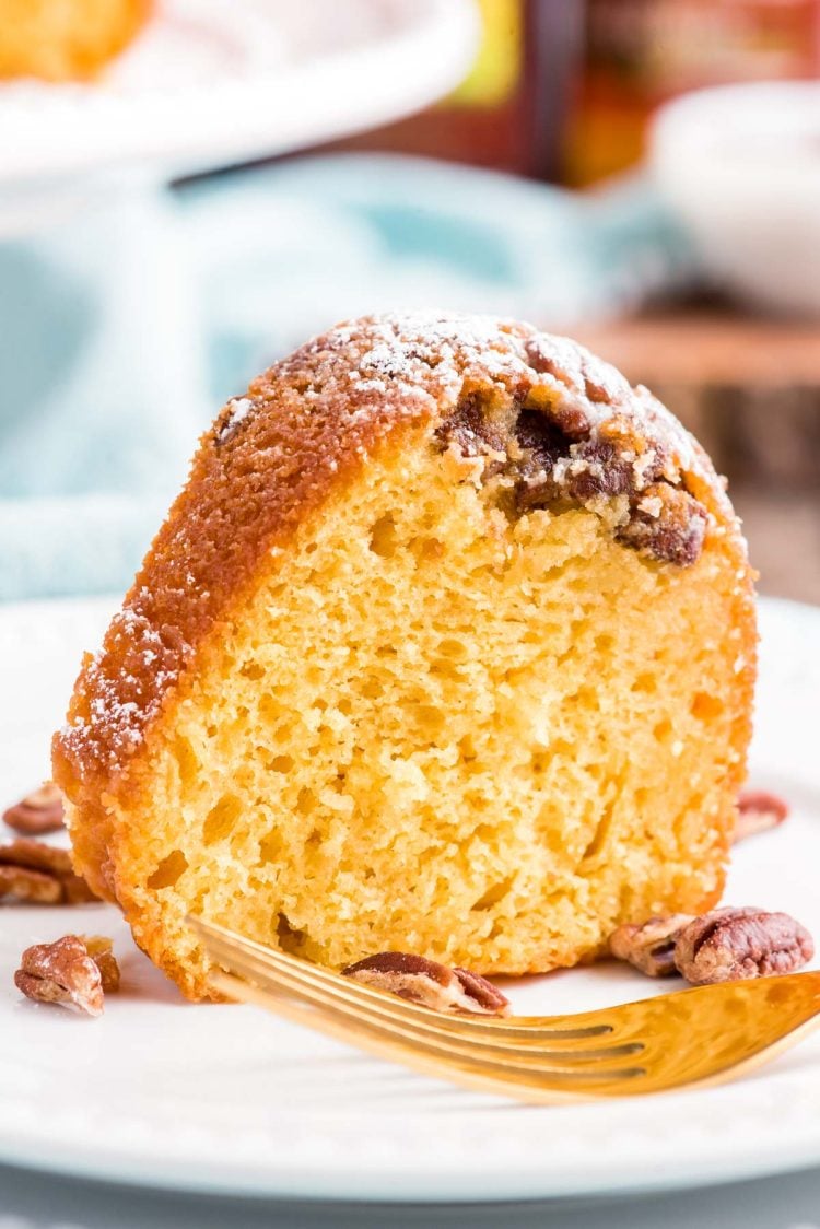 Close up photo of a slice of rum cake on a white plate with a blue napkin in the background.