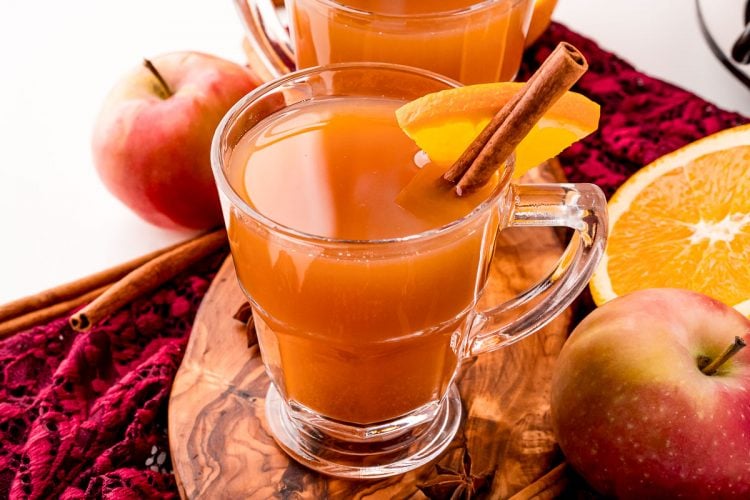 A mug of mulled apple cider on a wooden cutting board garnished with a cinnamon stick and orange slice.