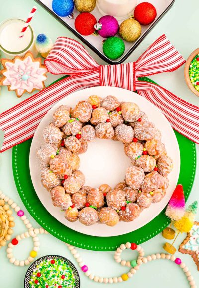 Overhead photo of a donut hole platter designed to look like a christmas wreath with holiday decorations scattered around it.