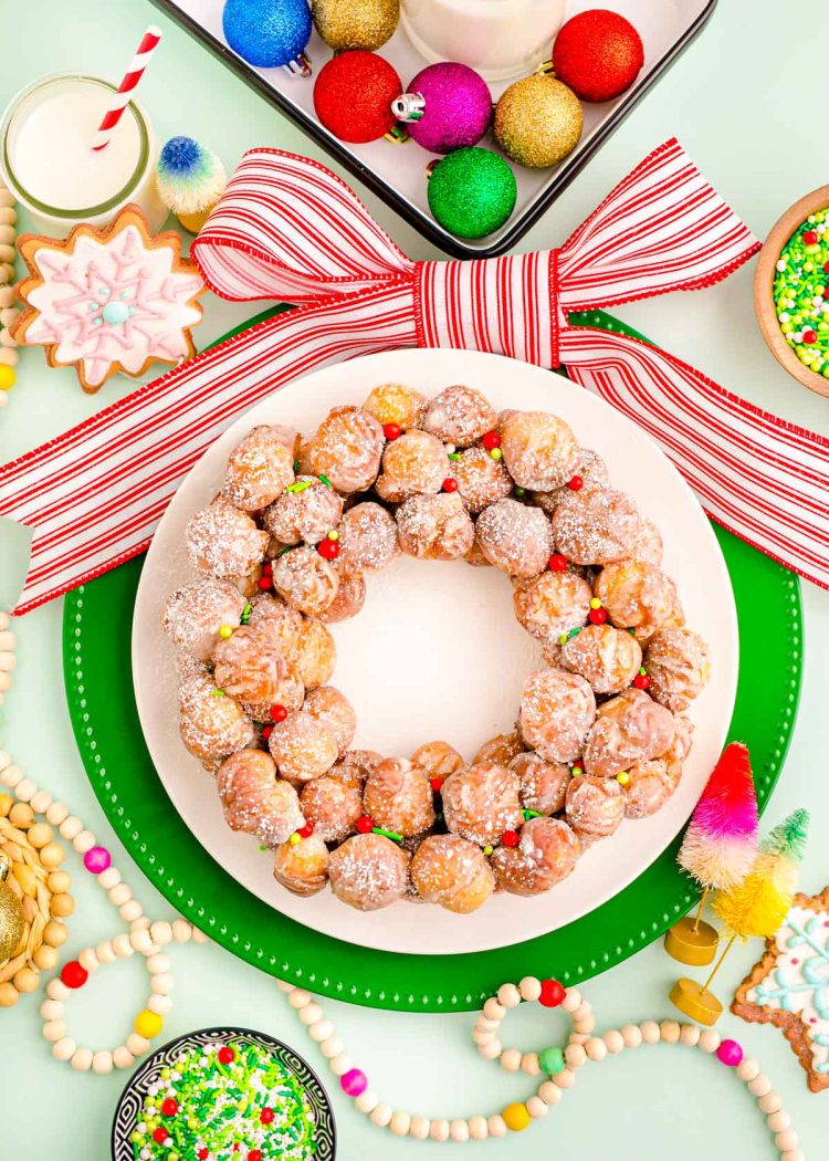 Overhead photo of a donut hole platter designed to look like a christmas wreath with holiday decorations scattered around it.