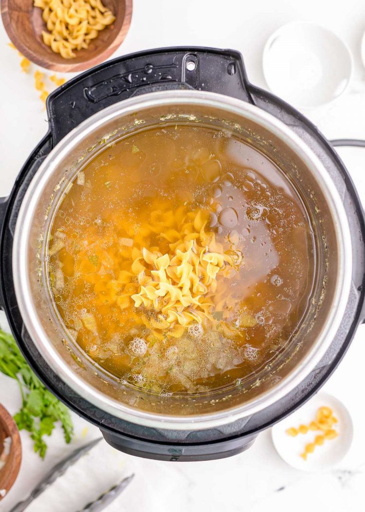 Egg noodles being added to an instant pot to make chicken noodle soup.