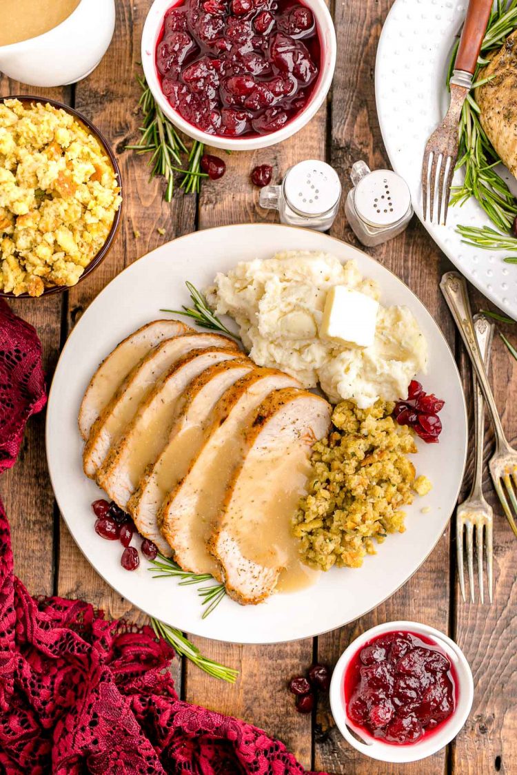 Overhead photo of a plate with a Thanksgiving dinner on it on a wooden table with side dishes and napkins around it.