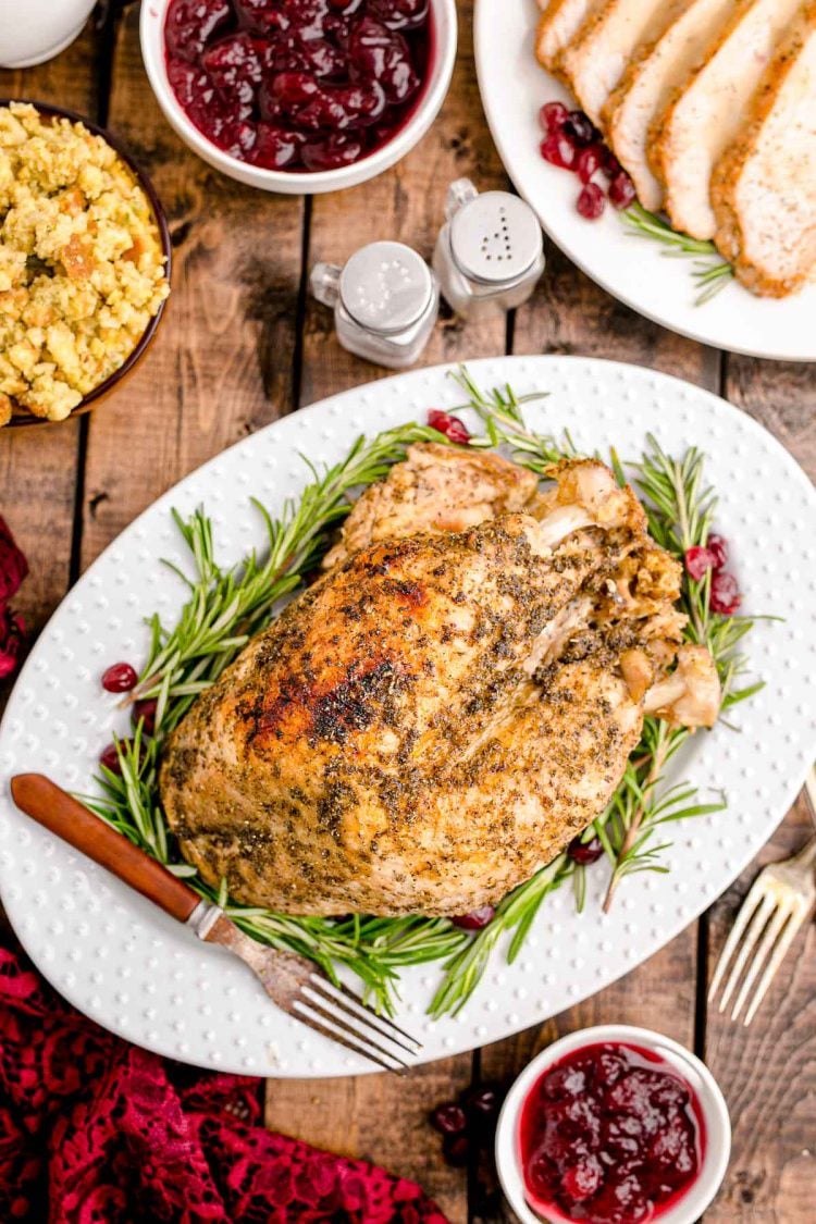 Overhead photo of a table ready for Thanksgiving with a turkey breast on a white platter and side dishes around it.