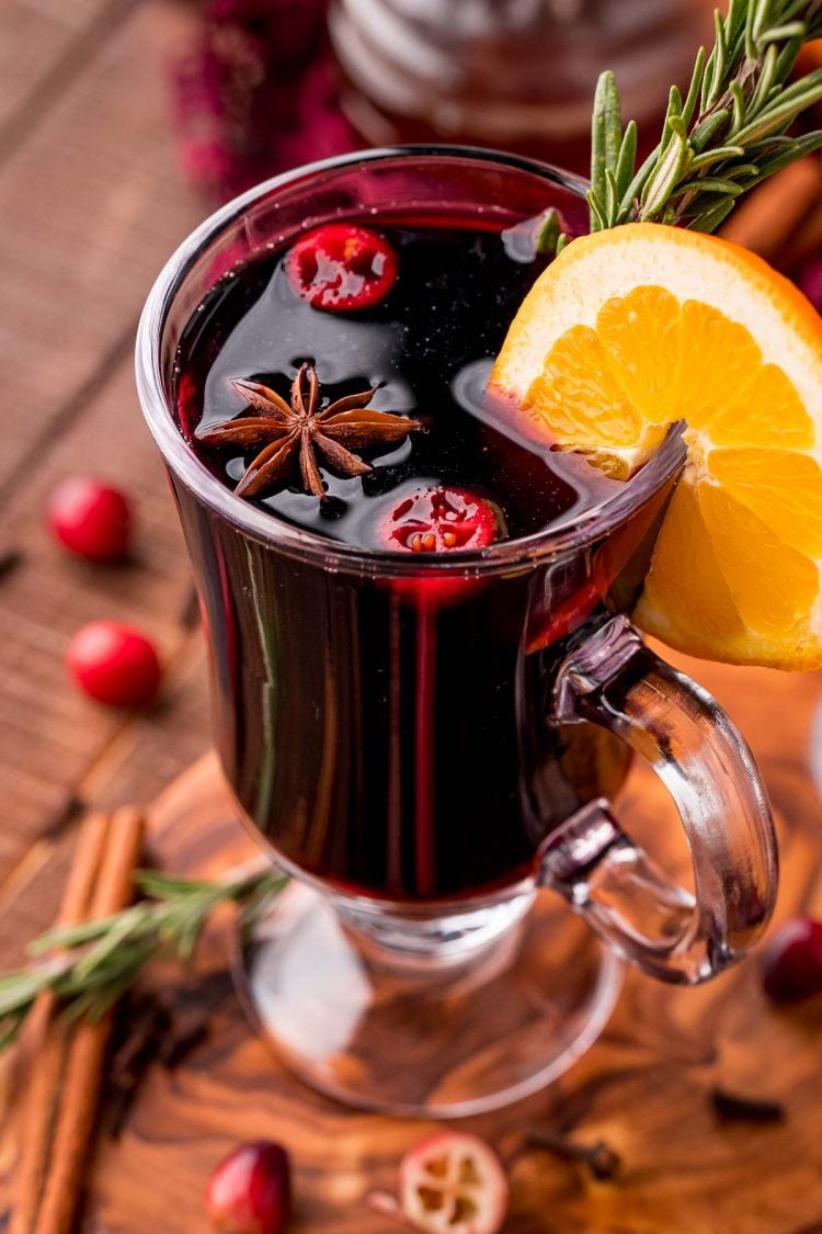 Close up photo of a glass mug filled with mulled wine garnished with rosemary and orange slice.